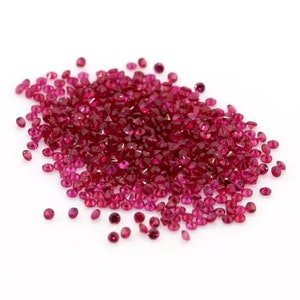 May include: A pile of loose red ruby gemstones, scattered on a white background.