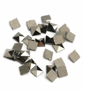 Könnte beinhalten: Eine Streuung von silberfarbenen quadratischen pyramidenförmigen Strasssteinen auf weißem Hintergrund.