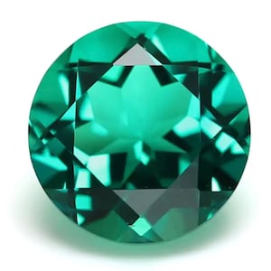 May include: A round, faceted emerald gemstone with a deep green color. The gemstone is cut to create a star-like pattern in the center.