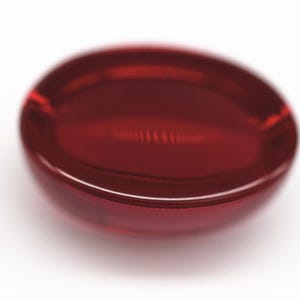 K&ouml;nnte beinhalten: Nahaufnahme eines tiefroten, oval geformten Objekts mit gl&auml;nzendem, transparentem Aussehen. Das Objekt befindet sich vor einem wei&szlig;en Hintergrund, der seine glatte, geschwungene Oberfl&auml;che hervorhebt. Die Farbe ist ein sattes, sattes Rot.