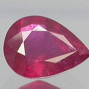May include: A pear-shaped ruby gemstone with a deep pink hue. The gemstone has a faceted cut and is set in a clear, transparent setting.