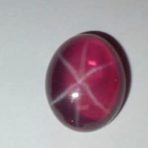 May include: A pink star ruby gemstone with a white star in the center.