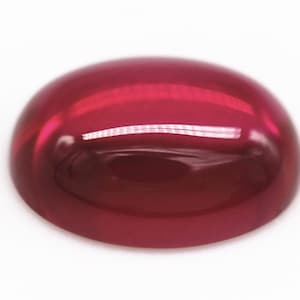 May include: A polished, oval-shaped gemstone with a deep red hue. The surface is smooth and reflective, with a slight dome shape. The gemstone appears to be translucent, allowing light to pass through. The overall appearance is glossy and vibrant.