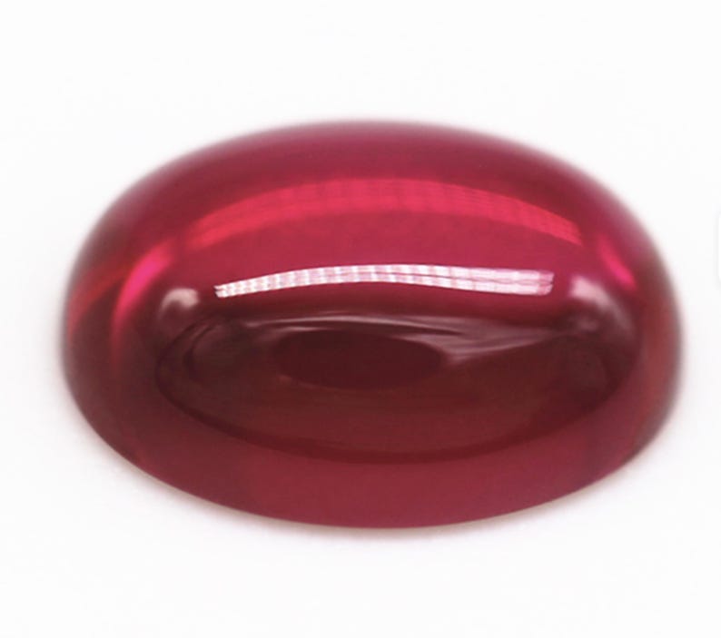 K&ouml;nnte beinhalten: Ein polierter, oval geformter Edelstein in tiefroter Farbe. Die Oberfl&auml;che ist glatt und reflektierend, leicht gew&ouml;lbt. Der Edelstein scheint durchscheinend zu sein und l&auml;sst Licht durch. Das Gesamtbild ist gl&auml;nzend und lebendig.