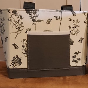 May include: Two tote bags with a floral print. The bags are made of a white fabric with a black floral design. The bags have brown handles and a brown bottom.