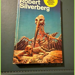 May include: A retro paperback book, "A Time of Changes" by Robert Silverberg, with a striking cover illustration of a skeletal creature. The book has a blue and orange backdrop and a yellow sticker proclaiming it a Nebula Award-winning novel.
