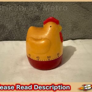 May include: A yellow chicken-shaped kitchen timer with a red comb and wattle. The base is red and features a circular dial with black printed numbers ranging from 40 to 55, indicating minutes. The timer has a smooth, rounded plastic body.