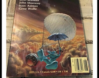 May include: A vintage paperback book cover for "The Magazine of Fantasy & Science Fiction," June 1985. The cover features a blue frog-like creature with a parachute and umbrella against a cloudy background. The magazine title and author names are visible.