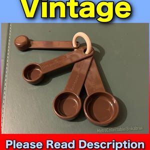 Può includere: Set di quattro cucchiaini dosatori in plastica marrone con un manico ad anello bianco. I cucchiaini sono etichettati 1/4 cucchiaino, 1/2 cucchiaino, 1 cucchiaino e 5 ml.