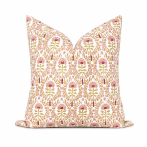 May include: A square throw cushion featuring a repeating floral pattern on a white background. The design consists of stylised pink and red flowers with yellow stems and leaves arranged in an intricate, symmetrical botanical motif across the fabric.