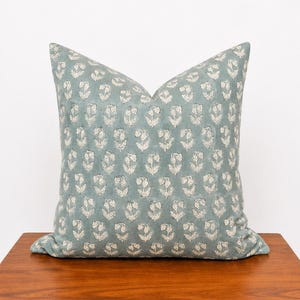 Könnte beinhalten: Ein quadratisches Zierkissen in gedämpftem Salbeigrün mit einem sich wiederholenden Muster aus kleinen, cremeweißen Blumenmotiven. Das Kissen hat eine weiche, strukturierte Optik mit einem durchgehenden Druck auf der gesamten Vorderseite.