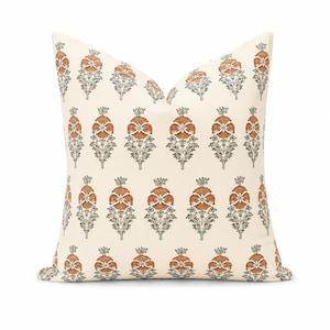 May include: A square throw pillow with an off-white base color featuring a repeating pattern of stylized floral motifs. The flowers are rendered in a burnt orange hue with dark gray stems and leaves, arranged in vertical rows across the fabric.