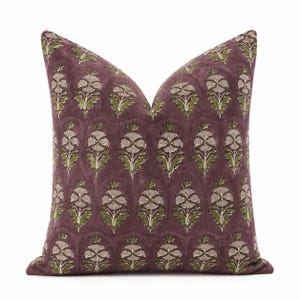 Puede incluir: Un cojín cuadrado con un fondo de color morado ciruela intenso y un patrón repetitivo de flores estilizadas en tonos beige y verde oliva. El diseño floral está dispuesto en columnas verticales por toda la superficie de la funda del cojín.