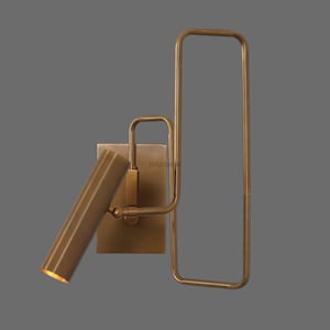 May include: A brass wall-mounted light fixture with a rectangular frame and a cylindrical shade that can be adjusted.