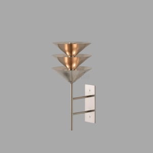 Op de afbeelding: Een moderne wandlamp met drie conische kappen. De kappen hebben zilver- en kopertinten en zijn verticaal gestapeld. De armatuur is gemonteerd op een zilveren metalen steel en een rechthoekige wandplaat.