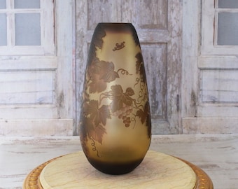May include: A gold-toned glass vase with a grapevine design. The vase is sitting on a round, gold-painted table with a marble top.