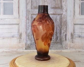 May include: A brown and amber glass vase with a raised design of leaves and fruit. The vase is sitting on a gold-painted table with a marble top.