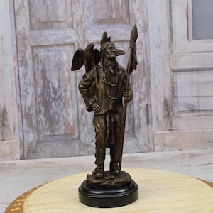 May include: Bronze sculpture of a Native American man holding a spear, wearing a feathered headdress and a necklace. The sculpture is on a black and white base.
