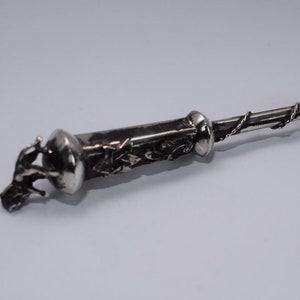 Może przedstawiać: Srebrne szczypce do cukru z ozdobnym wzorem winorośli i liści. Szczypce mają okrągły uchwyt z detalicznym wzorem ptaka.