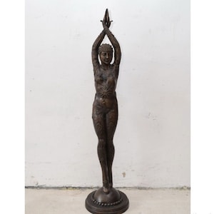 May include: A bronze sculpture of a woman standing with her arms raised above her head. The sculpture is detailed with intricate patterns and designs.