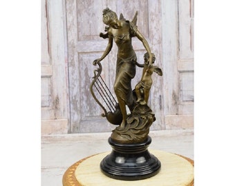 May include: Bronze sculpture of a woman playing a lyre with a cherub beside her. The sculpture is on a black marble base.