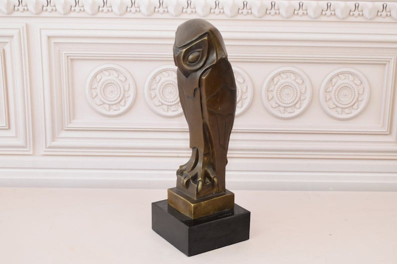 May include: A bronze sculpture of an owl with a geometric design. The owl is perched on a black base.