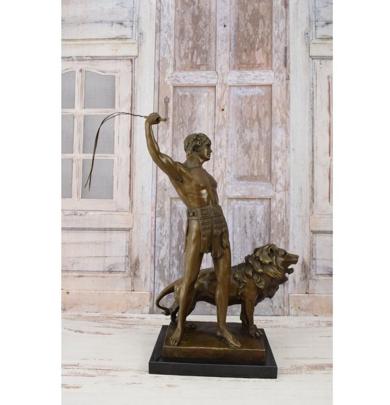 May include: Bronze sculpture of a man holding a whip standing next to a lion. The sculpture is on a black base.