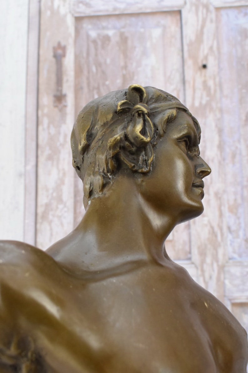 May include: Bronze sculpture of a person's bust, the person is facing to the right, with a detailed head and neck, and a smooth, polished surface.