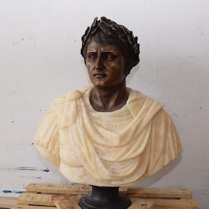 Könnte beinhalten: Eine Bronzestatue eines Mannes mit einem Lorbeerkranz auf dem Kopf. Die Büste steht auf einem schwarzen Marmorsockel.