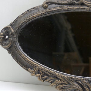 May include: An oval-shaped, ornate, black cast iron mirror with a decorative, gold-painted floral design.