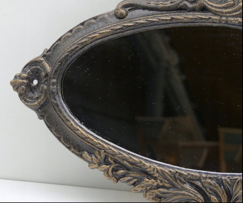 May include: An oval-shaped, ornate, black cast iron mirror with a decorative, gold-painted floral design.