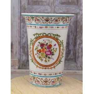 Op de afbeelding: Een witte keramische vaas met een bloemenmotief. De vaas heeft een brede opening en een smalle basis. Het bloemenmotief is in tinten roze, oranje en groen. De vaas is versierd met een gouden rand.