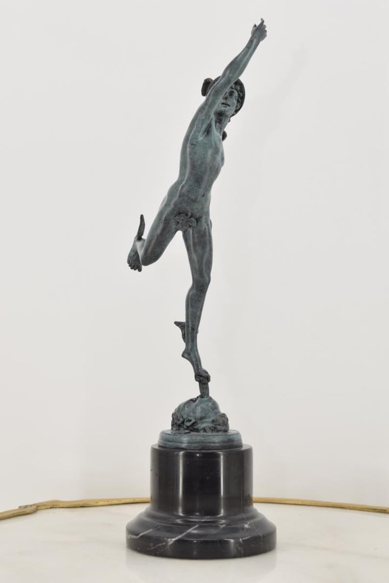 May include: A bronze statue of a male figure in a dynamic pose, with one arm raised and the other leg extended. The statue is mounted on a black marble base, showcasing classical art.