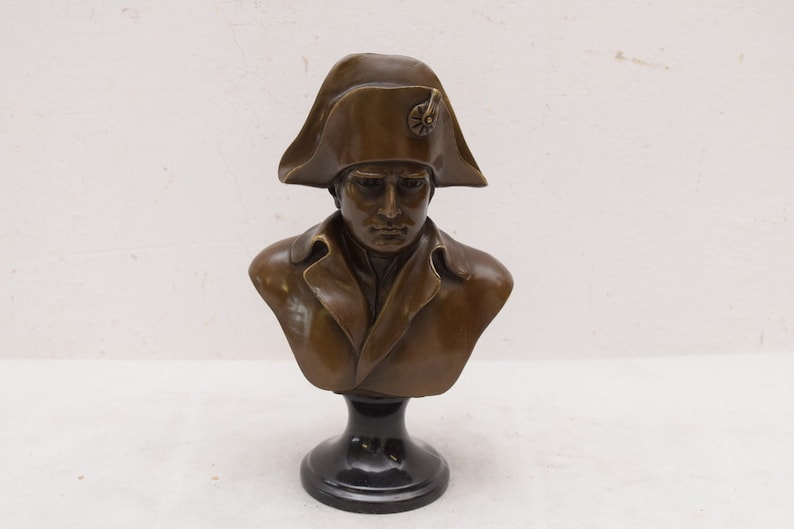 May include: Bronze bust sculpture of Napoleon Bonaparte wearing a bicorne hat on a black pedestal.