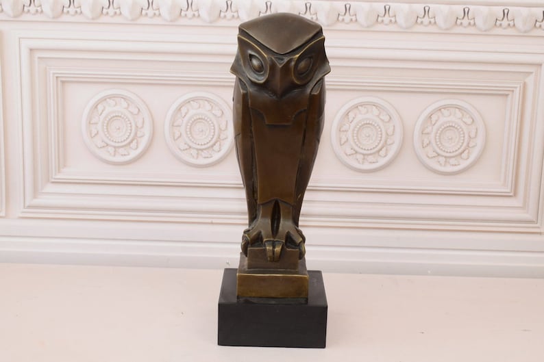 May include: A bronze sculpture of an owl with a geometric design. The owl is standing on a square base with a black marble base.