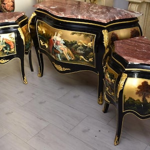 Puede incluir: Un conjunto de tres muebles antiguos pintados de negro con detalles dorados y tapas de mármol. Las piezas incluyen una cómoda grande y dos mesas auxiliares más pequeñas, cada una con escenas pintadas a mano.
