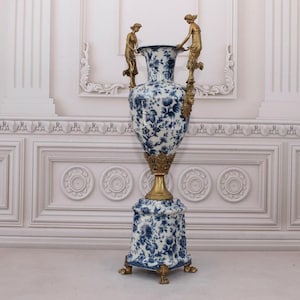 May include: A large, blue and white porcelain vase with gold accents and two gold figures on the sides. The vase is on a pedestal with a matching design.