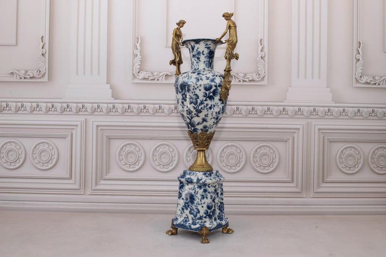 May include: A large, blue and white porcelain vase with gold accents and two gold figures on the sides. The vase is on a pedestal with a matching design.