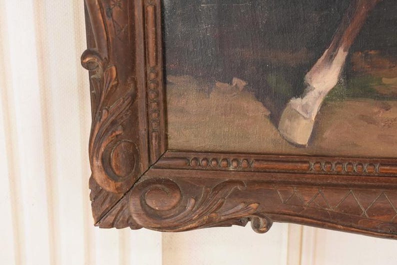 Pu&ograve; includere: Un angolo di un dipinto incorniciato con la gamba e lo zoccolo di un cavallo. Il dipinto &egrave; in una cornice di legno scuro e ornata con dettagli intagliati. L'opera d'arte raffigura un cavallo in un ambiente naturale, con toni tenui di marrone, beige e verde.