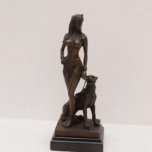 May include: Bronze sculpture of a woman in an Egyptian-inspired outfit standing with a panther on a black base.