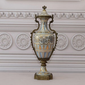 May include: A large, ornate porcelain vase with gold and blue accents. The vase has a decorative design and is mounted on a bronze base.