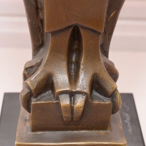 May include: Close-up of the base of a bronze sculpture. The sculpture has a geometric design and is resting on a black base.