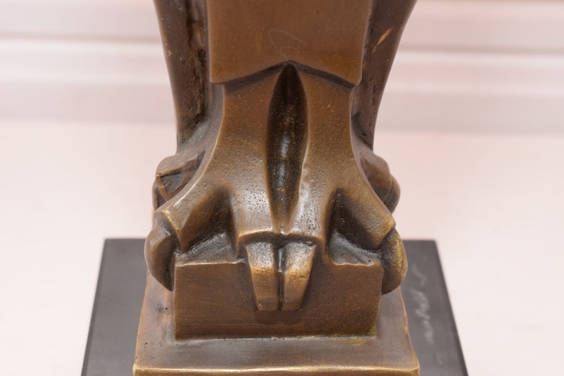May include: Close-up of the base of a bronze sculpture. The sculpture has a geometric design and is resting on a black base.