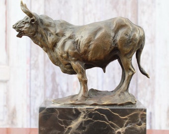 Puede incluir: Escultura de bronce de un toro de pie sobre una base de mármol negro. El toro está mirando hacia la izquierda y tiene una musculatura imponente. La escultura es de estilo tradicional.
