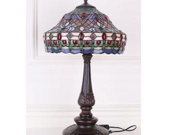 May include: A stained glass table lamp with a brown base and a multi-colored shade featuring geometric patterns and red accents.