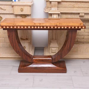 Puede incluir: Una consola de madera con tapa rectangular y patas curvas. La tapa es de color marrón claro con borde decorativo, y las patas son de color marrón oscuro. La mesa mide aproximadamente 152 cm de largo y 76 cm de alto.