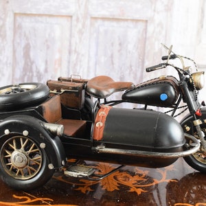 May include: Black and brown vintage-style motorcycle with a sidecar. The motorcycle features a brown leather seat, luggage, and a spare tire. The wheels have a gold finish, and the sidecar has a footrest.