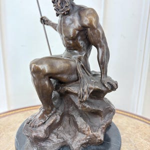 May include: Bronze sculpture of a seated male figure with a beard, holding a trident. The figure is atop a rocky base, mounted on a black marble circular base. The sculpture is a detailed representation of a mythological or historical figure.