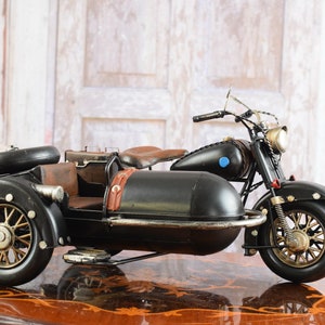 May include: A black and brown vintage motorcycle with a sidecar. The motorcycle has a black body, brown seat, and gold-colored wheels. The sidecar is attached to the right side of the motorcycle. The motorcycle is a decorative item.