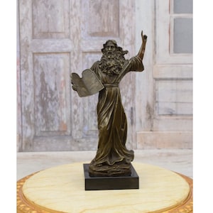May include: Bronze sculpture of a man holding a scroll and raising his right hand. The sculpture is on a black marble base.